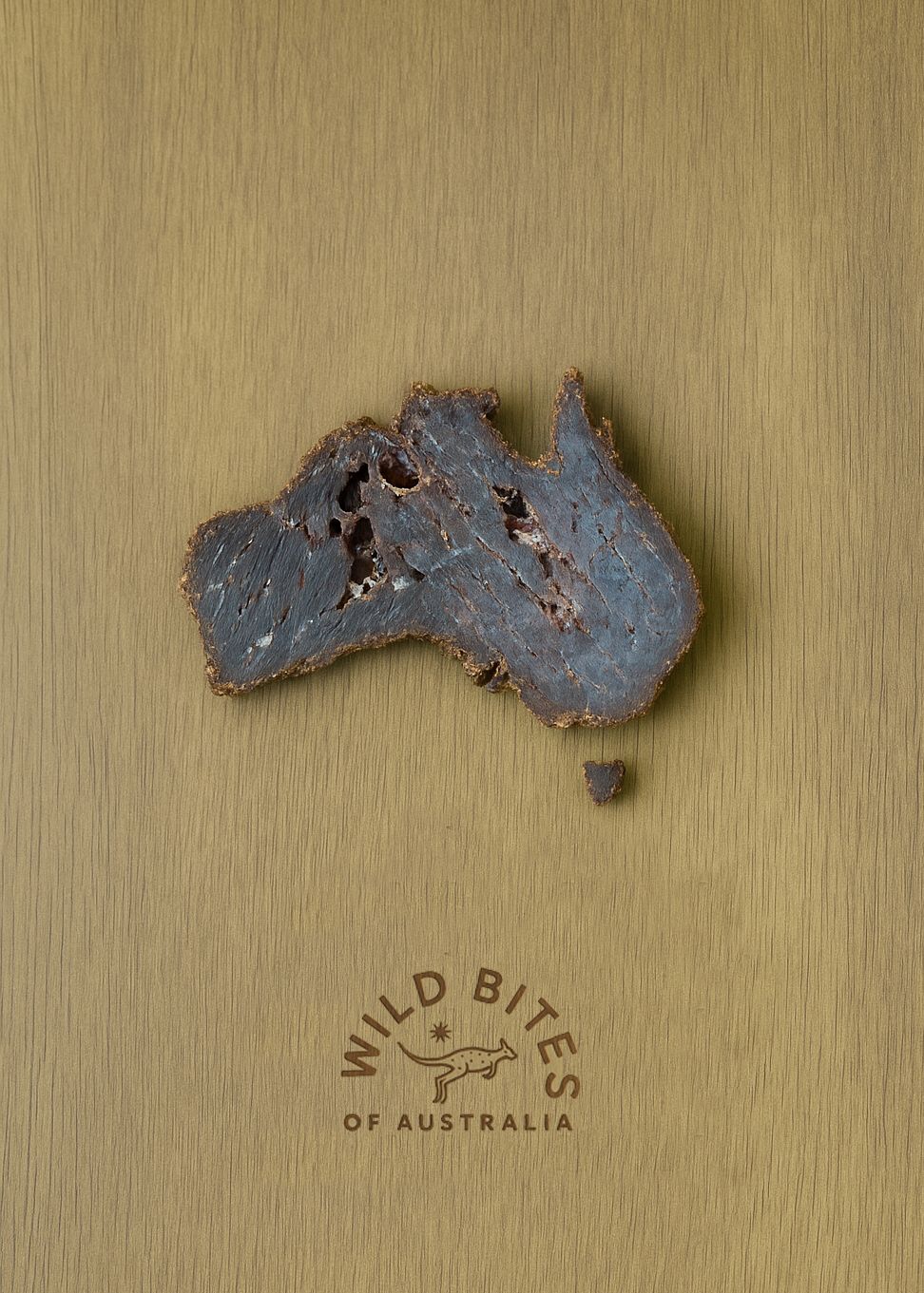 Map of Australia made from a kangaroo biltong piece on a wooden surface with 'Wild Bites of Australia' branding.